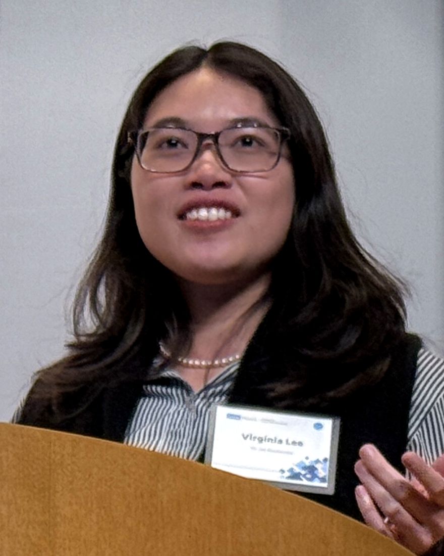 Dr. Virginia Lee speaking at a lectern, smiling and mid gesture